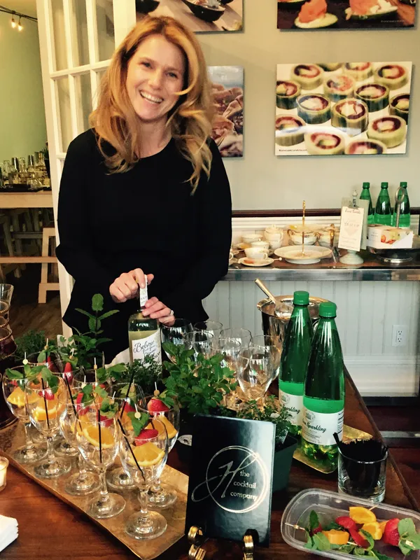 Gina Weinstein smiling behind a table set with cocktails, fresh herbs and glassware